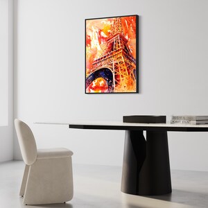 May include: A watercolor painting of the Eiffel Tower in shades of orange, red, and yellow. The painting is framed in black and hanging on a white wall above a modern dining table.