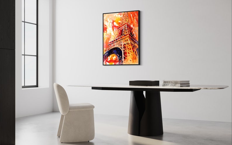 May include: A watercolor painting of the Eiffel Tower in shades of orange, red, and yellow. The painting is framed in black and hanging on a white wall above a modern dining table.