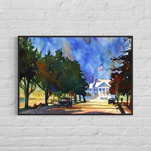 May include: Watercolor painting of a white building with columns and an American flag, framed in black. The artwork depicts a street scene with trees, cars, and a blue sky.