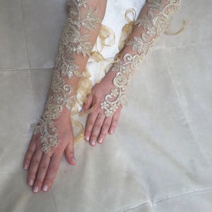 May include: A pair of long, ivory lace gloves with delicate floral patterns and a sheer fabric. The gloves are tied with a ribbon at the wrist.