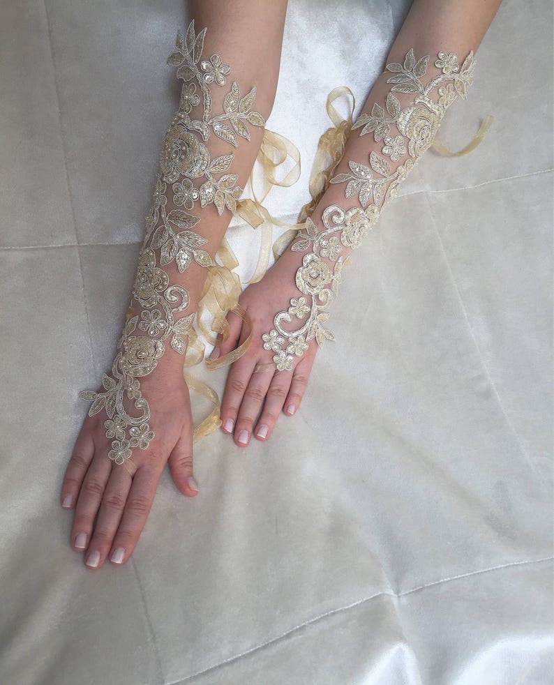 May include: A pair of long, ivory lace gloves with delicate floral patterns and a sheer fabric. The gloves are tied with a ribbon at the wrist.