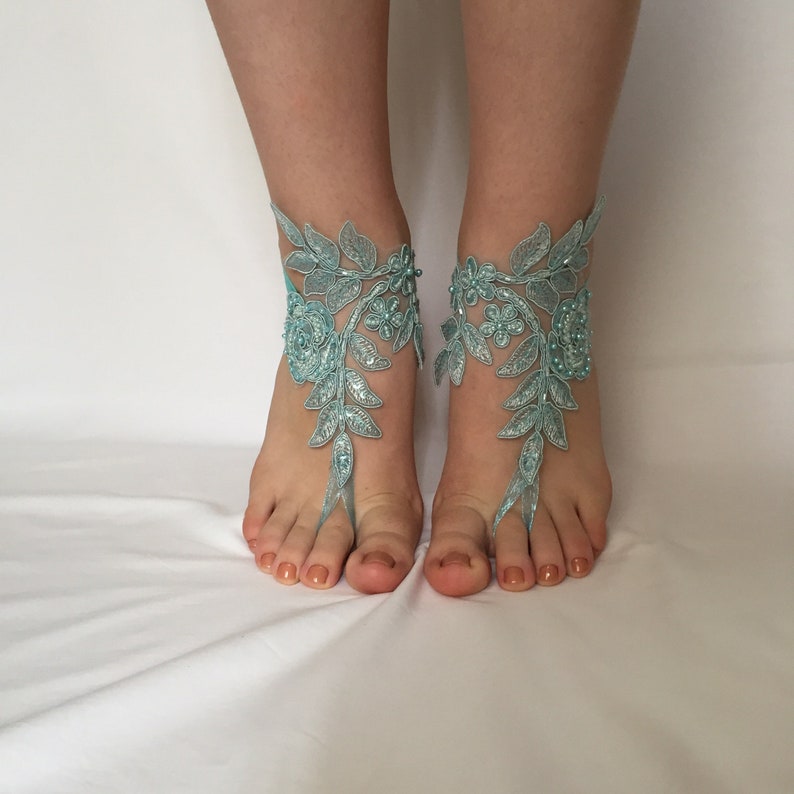 May include: A pair of light blue floral lace barefoot sandals with beaded accents.