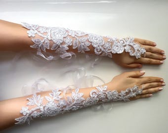 Puede incluir: Un par de guantes sin dedos de encaje blanco con intrincados bordados florales, adornos de lentejuelas y delicadas cuentas. Los guantes se extienden hasta el antebrazo e incluyen cintas blancas finas para un ajuste seguro en la muñeca.