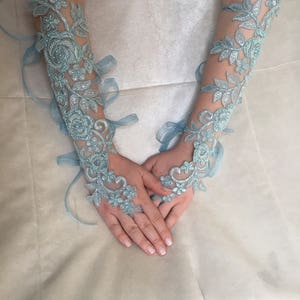 May include: A pair of light blue lace gloves with floral designs. The gloves are tied with matching ribbons.