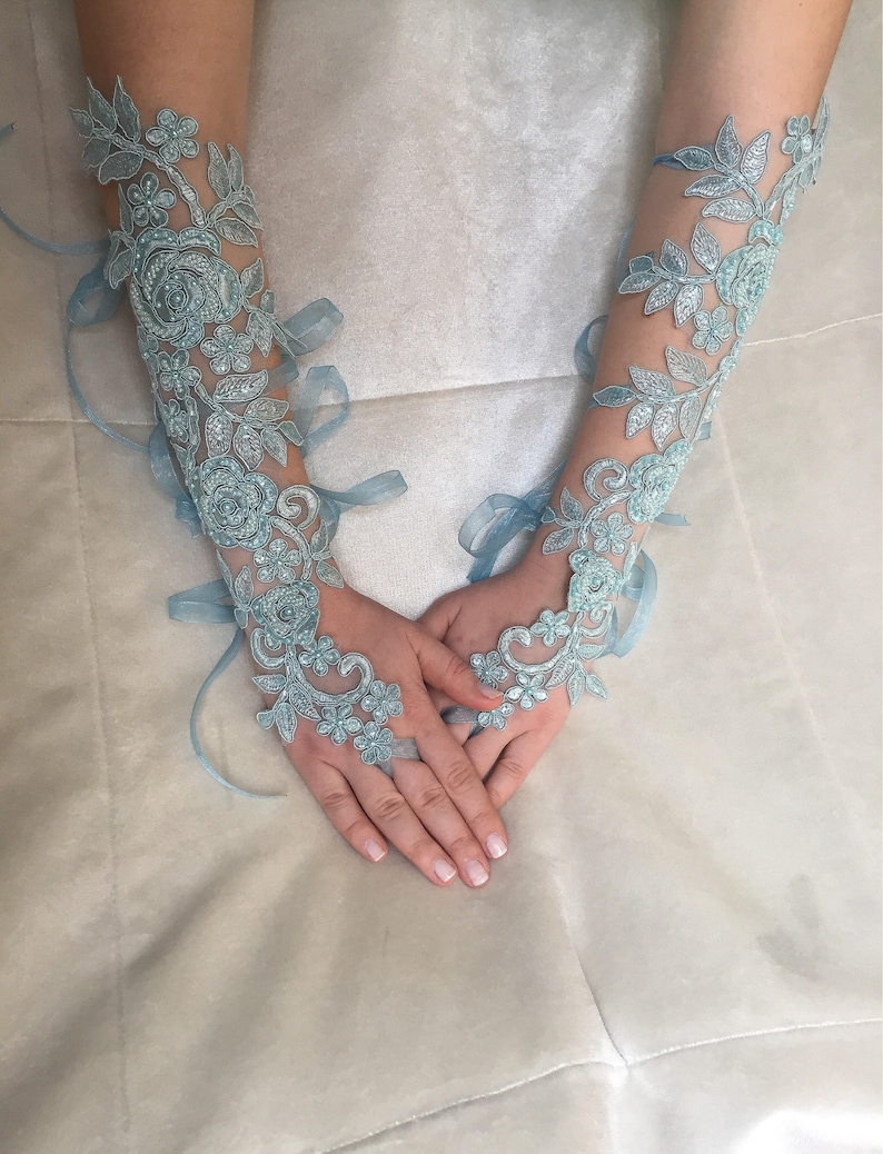 May include: A pair of light blue lace gloves with floral designs. The gloves are tied with matching ribbons.