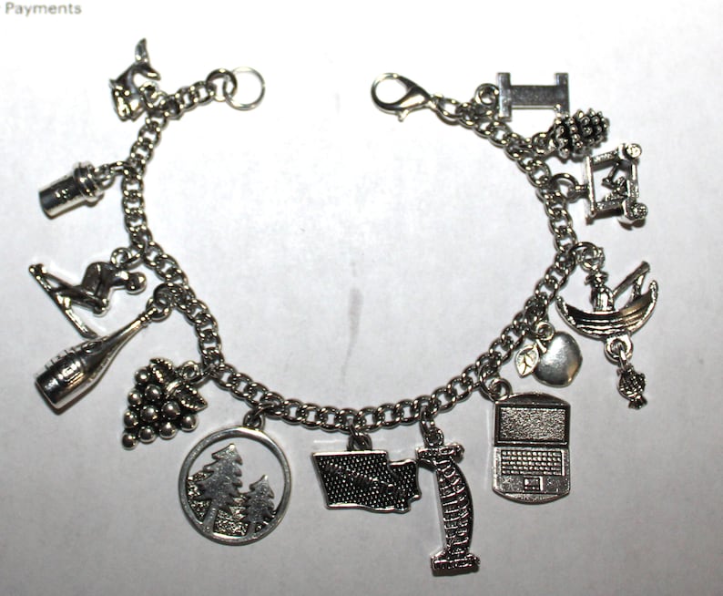 May include: A silver charm bracelet with various charms, including a wine bottle, grapes, a skiier, a pine tree, a laptop, an apple, a boat, a building, and a state outline.
