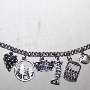 May include: A silver charm bracelet with various charms, including a wine bottle, grapes, a skiier, a tree, a state outline, a lighthouse, a radio, an apple, and a boat.