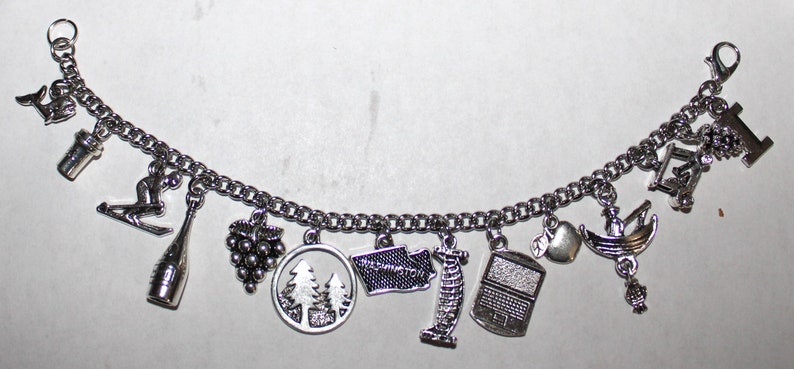 May include: A silver charm bracelet with various charms, including a wine bottle, grapes, a skiier, a tree, a state outline, a lighthouse, a radio, an apple, and a boat.