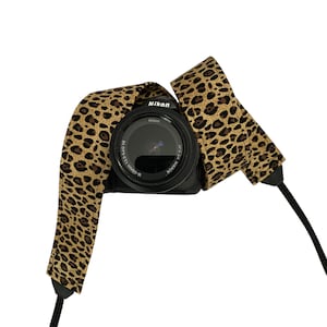 May include: A black camera with a leopard print camera strap. The camera lens says "Nikon AF-S DX NIKKOR 18-55mm 1:3.5-5.6G IF ED".