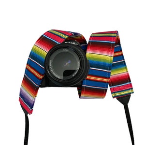 May include: A black Nikon camera with a colorful striped camera strap. The strap features a vibrant pattern of red, blue, yellow, and green stripes. The camera lens is visible, and the strap is attached to the camera body.