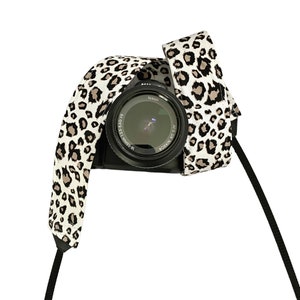 May include: A black camera with a leopard print camera strap. The camera lens says "Nikon AF-S DX NIKKOR 18-55mm 1:3.5-5.6G VR".