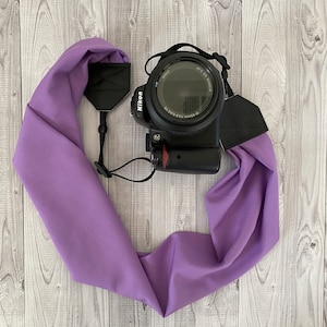May include: A purple camera strap made of fabric with black adjustable straps and a camera attached.