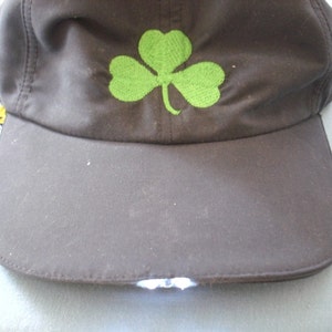 May include: A black baseball cap with a green shamrock embroidered on the front. The cap has a built-in LED light on the brim.