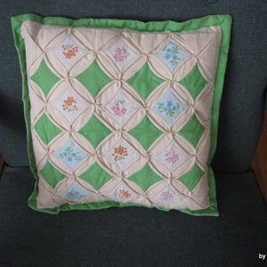 May include: A green and white quilted pillow with a diamond pattern and floral embroidery. The pillow is sitting on a green armchair.
