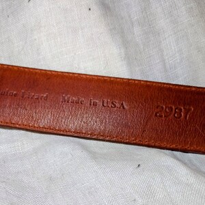 May include: Close-up of a brown leather belt with the text "Genuine Lizard Made in U.S.A. 2987" embossed on the back.
