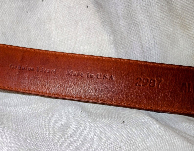 May include: Close-up of a brown leather belt with the text "Genuine Lizard Made in U.S.A. 2987" embossed on the back.
