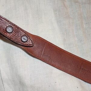 May include: Brown leather belt with a textured surface and three metal rivets. The belt is labeled "Genuine Lizard Skin Made in Italy."