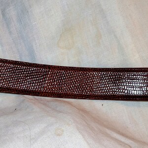 May include: A brown leather belt with a textured, lizard-like pattern.