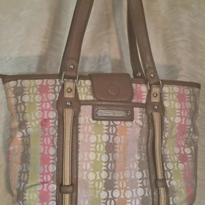 May include: A patterned tote bag with brown leather handles and trim. The bag features a repeating circle pattern in pink, green, orange, and white. It has a flap closure and a small metal plaque with text.