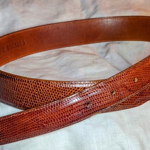 May include: A brown leather belt with a textured snakeskin pattern. The belt is made by "J.F.J.S. BUCKLES".