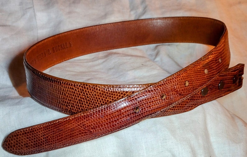May include: A brown leather belt with a textured snakeskin pattern. The belt is made by "J.F.J.S. BUCKLES".