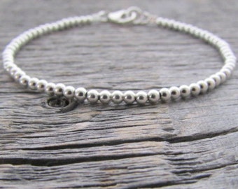 Puede incluir: Un brazalete de plata con un diseño sencillo. El brazalete está hecho de pequeñas cuentas redondas que están espaciadas uniformemente.