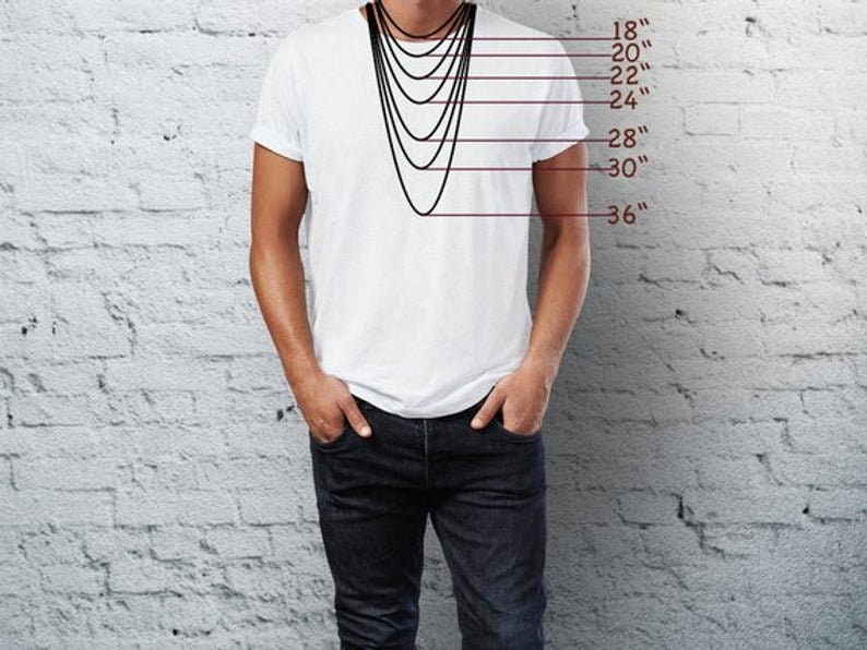 Puede incluir: Un hombre con una camiseta blanca y pantalones vaqueros azules est&aacute; de pie frente a una pared de ladrillo blanco. Un collar negro cuelga de su cuello, con diferentes longitudes marcadas en pulgadas de 18 a 36 pulgadas.