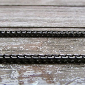 Puede incluir: Dos cadenas de metal negro sobre una superficie de madera. Las cadenas est&aacute;n hechas de peque&ntilde;os eslabones entrelazados.