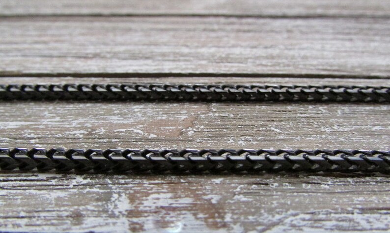 Puede incluir: Dos cadenas de metal negro sobre una superficie de madera. Las cadenas est&aacute;n hechas de peque&ntilde;os eslabones entrelazados.