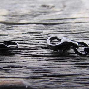 Puede incluir: Una cadena de metal negro con un cierre de mosquet&oacute;n. La cadena est&aacute; sobre una superficie de madera.