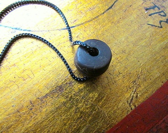 May include: A dark brown stone bead with a hole in the center, strung on a black chain. The bead is on a gold background with black markings.