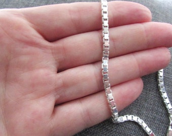 Op de afbeelding: Een zilveren ketting met een box chain ontwerp. De ketting ligt op de hand van een persoon.