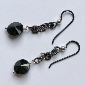 May include: A pair of black earrings with black crystal beads and silver accents. The earrings have a delicate chain design and are made with black wire.