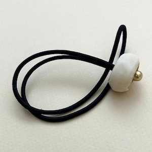 Puede incluir: Una liga para el pelo negra con una cuenta de cerámica blanca y un acento dorado.