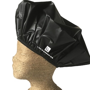 May include: A black shower cap with the text "LOC:CESSORIES" in white. The cap is made of a shiny, waterproof material and is displayed on a mannequin head.