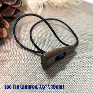 May include: A wooden loc tie with a dark brown finish and a black elastic band. The loc tie is approximately 7.5 inches (19 cm) long. The wooden toggle has a rectangular shape with a hole for the elastic.