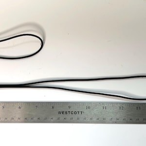 May include: Two brown leather and metal key fobs with black cords. One fob is approximately 4 inches long, and the other is approximately 10 inches long. A stainless steel ruler is in the image for scale.