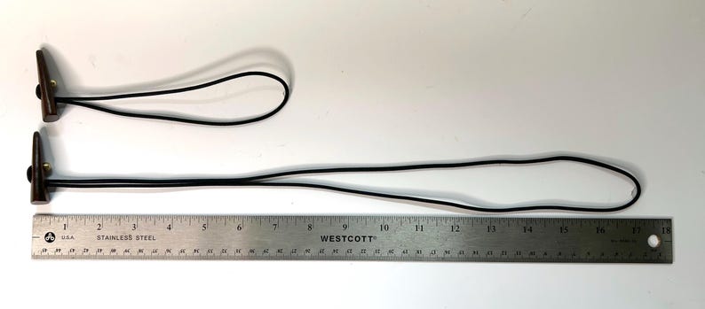 May include: Two brown leather and metal key fobs with black cords. One fob is approximately 4 inches long, and the other is approximately 10 inches long. A stainless steel ruler is in the image for scale.
