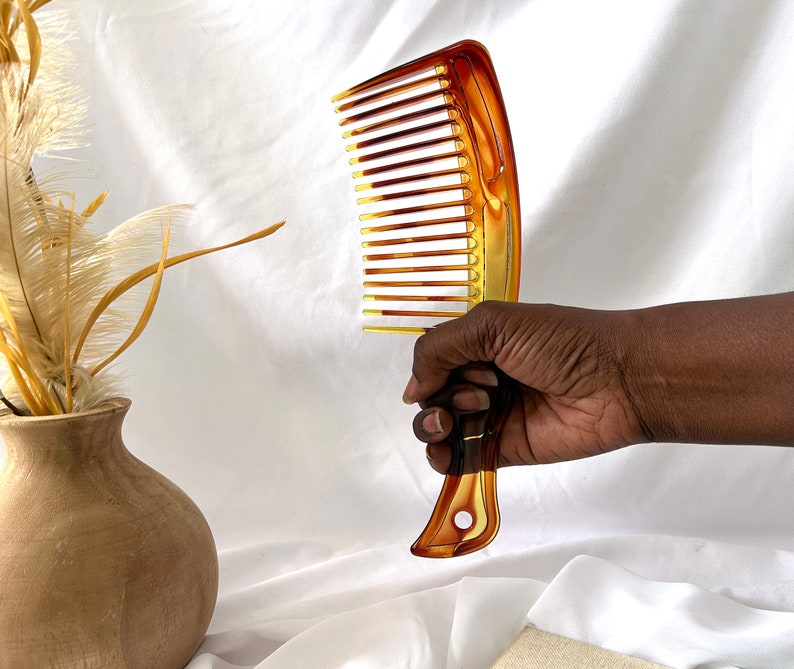 May include: A brown and amber plastic comb with wide teeth. The comb is held in a hand.