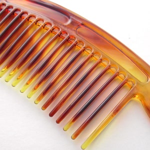 May include: A brown plastic comb with a wide tooth design. The comb has a curved handle and is made of a translucent material.