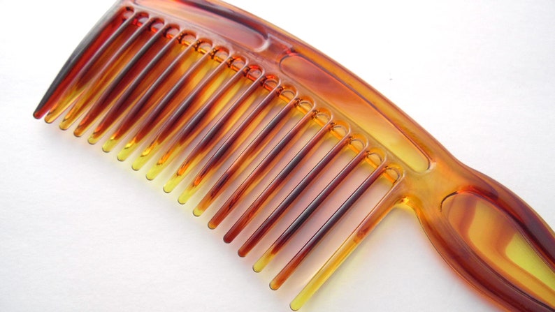 May include: A brown plastic comb with a wide tooth design. The comb has a curved handle and is made of a translucent material.