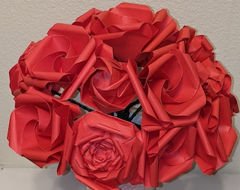 May include: A bouquet of red paper roses in a clear glass vase with a pink and white patterned liner.