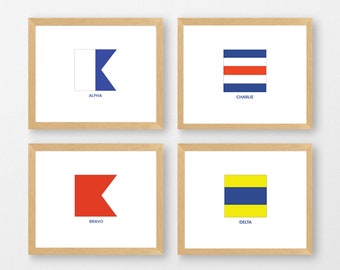 May include: Four framed prints of nautical signal flags. Each print features a different flag with its corresponding letter and name: Alpha, Bravo, Charlie, and Delta. The flags are white, red, blue, and yellow.