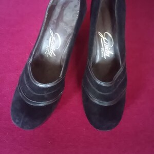May include: Pair of black suede heeled shoes with a gold inscription that reads "Linda Shoes".