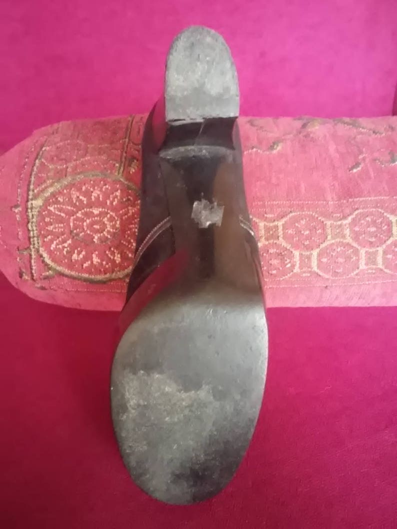 May include: Close-up of the bottom of a black leather heeled shoe. The sole is worn and has a slight scuff mark.