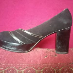 May include: Black suede platform heels with a thick, block heel. The shoes have a silver trim detail around the platform and the heel.