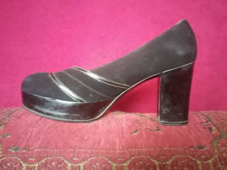 May include: Black suede platform heels with a thick, block heel. The shoes have a silver trim detail around the platform and the heel.