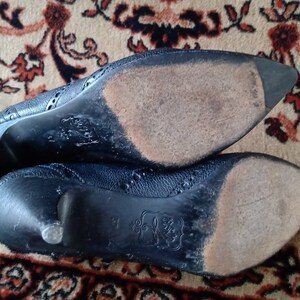 Puede incluir: Primer plano de las suelas de dos zapatos de tac&oacute;n de cuero negro. Los zapatos tienen un patr&oacute;n decorativo y un aspecto desgastado.
