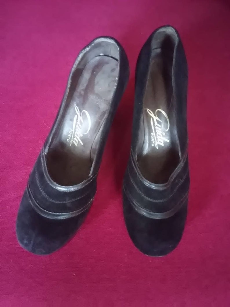 May include: Pair of black suede heeled shoes with a gold inscription that reads "Linda Shoes".