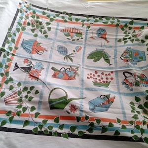 Op de afbeelding: Witte tafelkleed met een herhalend rasterpatroon met illustraties met een tuinthema in oranje, blauw en groen. De rand heeft een groen wijnstokontwerp met bladeren. Het tafelkleed is gemaakt van een zacht, waarschijnlijk katoenen materiaal.